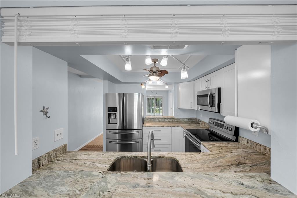 Kitchen featuring a double stainless steel sink, stone countertops with a matching backsplash, white cabinetry with stainless steel hardware, and a suite of stainless steel appliances