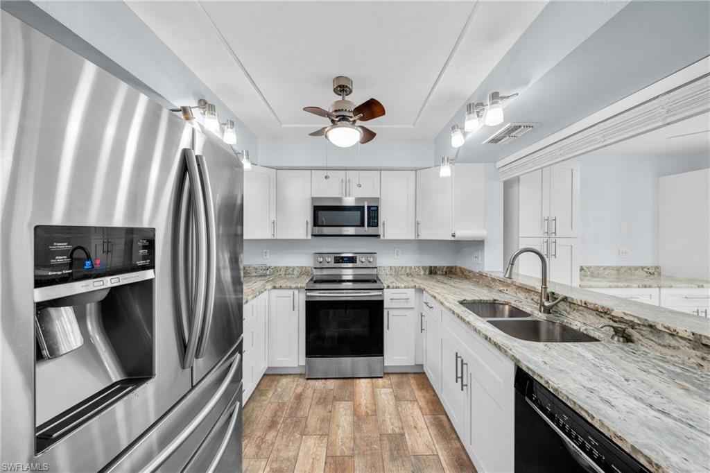 Modern kitchen featuring stainless steel appliances, white cabinetry, wood-finish flooring, light-toned countertops, and a dual basin sink