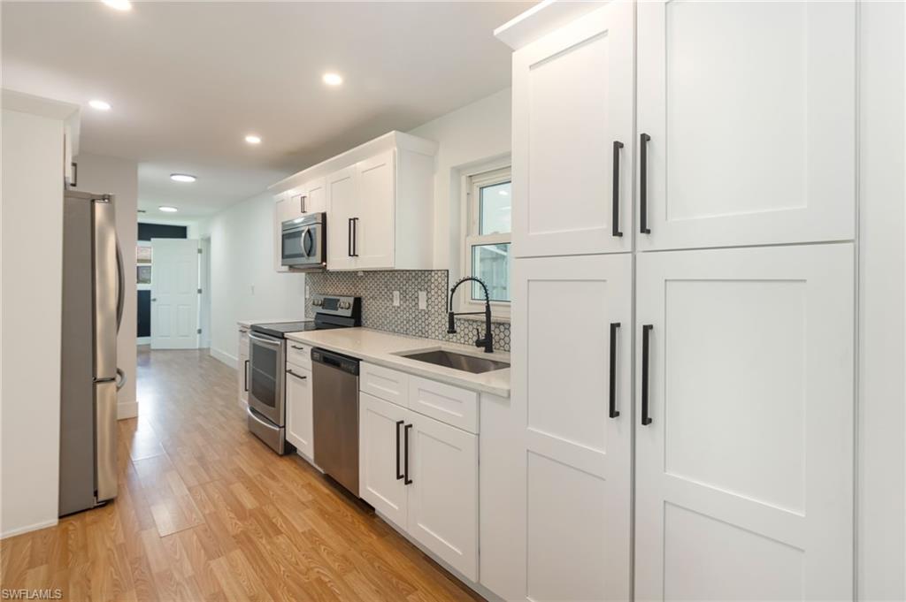 White shaker cabinetry with matte black hardware, stainless steel appliances, stone countertops, and a patterned tile backsplash