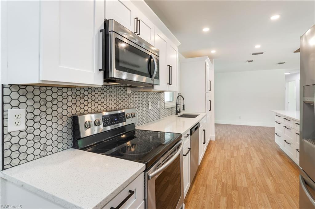 Modern kitchen featuring white shaker cabinetry, stainless steel appliances including a microwave and range, light-toned countertops, and a white hexagon tile backsplash