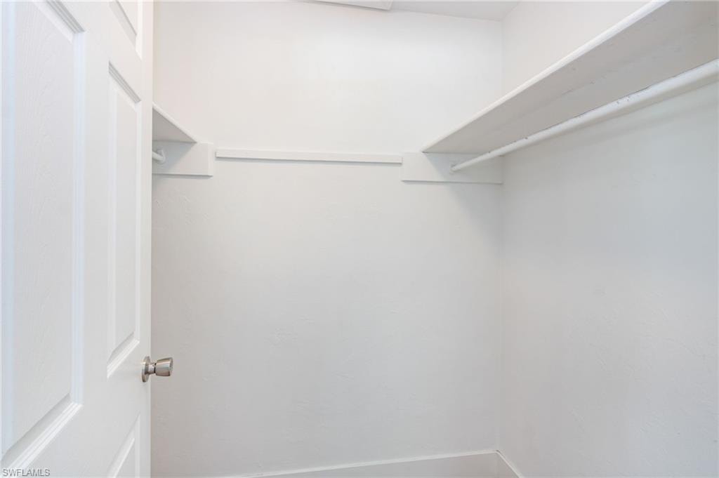 White door with brushed nickel hardware opens to a bright closet featuring white shelving and a hanging rod
