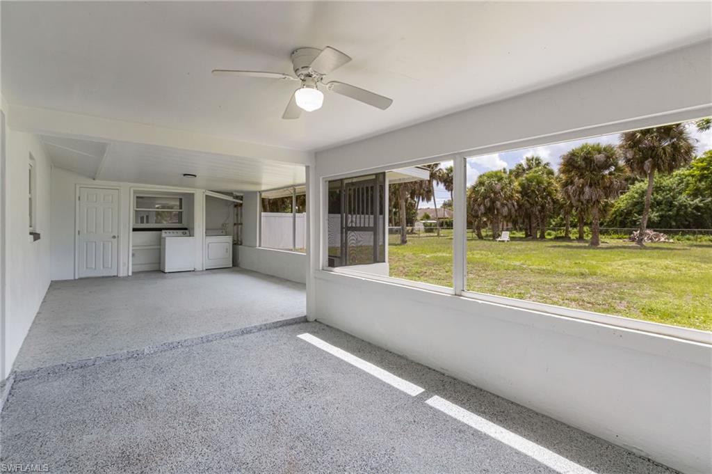 Screened-in patio with textured gray flooring, ceiling fan, and expansive views of the green landscape and palm trees