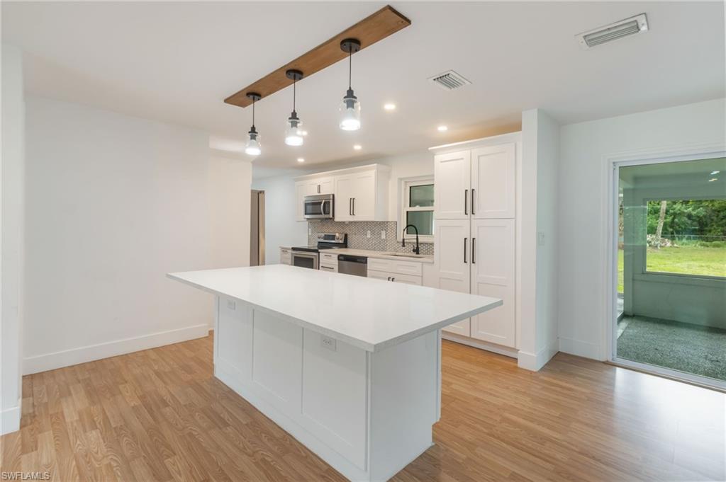 Kitchen featuring a large central island with a white countertop, wood-finish flooring, white cabinetry with dark hardware, recessed lighting, and a sliding glass door to an outdoor area