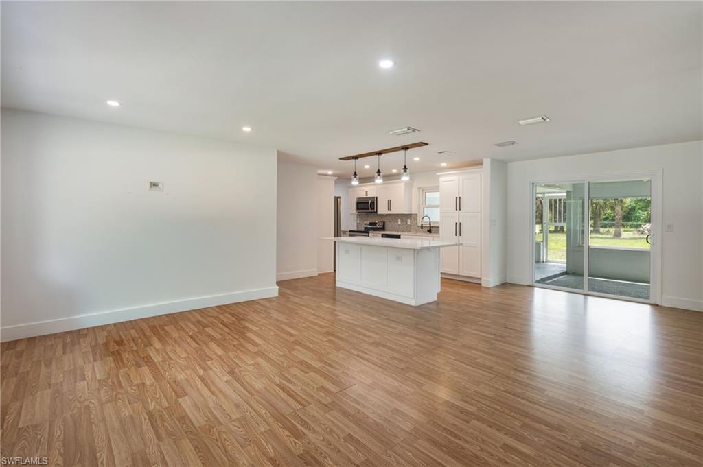 Bright open-concept interior featuring wood-finish flooring, recessed lighting, a kitchen island with seating, a modern pendant light fixture, and sliding glass doors to the exterior