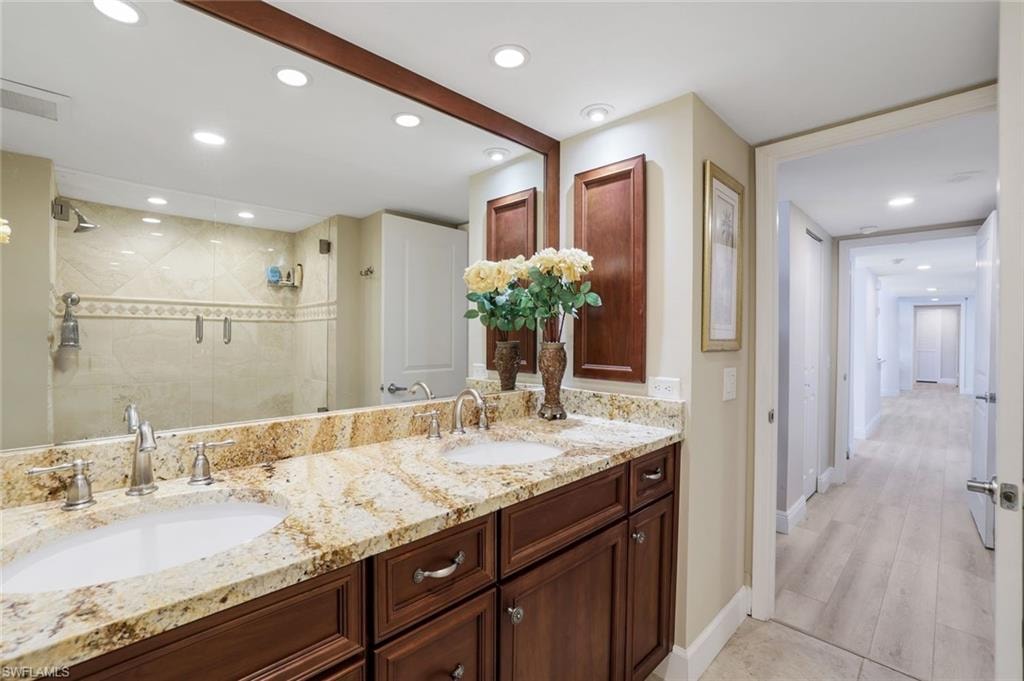 Bathroom with double vanity, a stall shower, baseboards, recessed lighting, and wood finished floors
