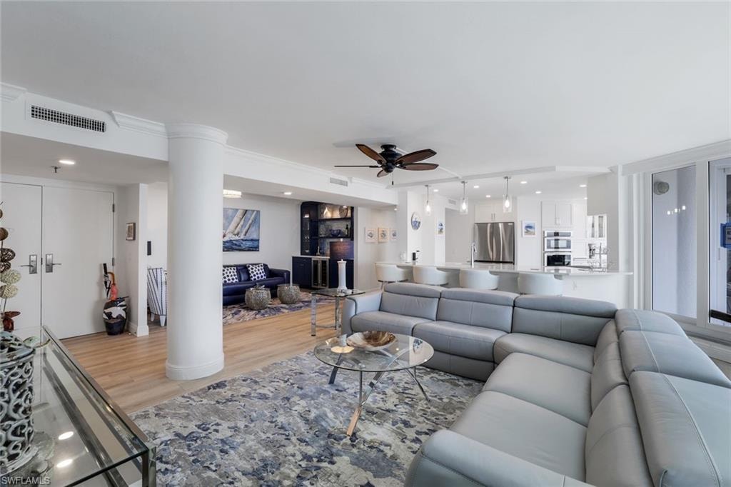 Living area with light wood finished floors, ceiling fan, ornate columns, and recessed lighting