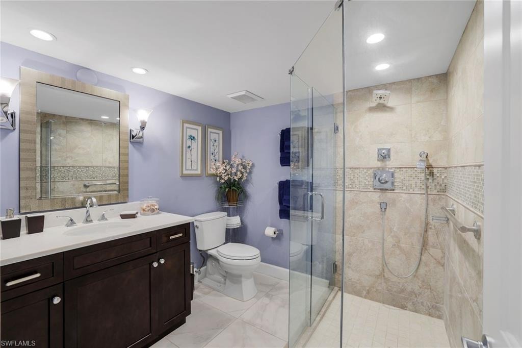 Bathroom featuring toilet, vanity, a stall shower, recessed lighting, and baseboards