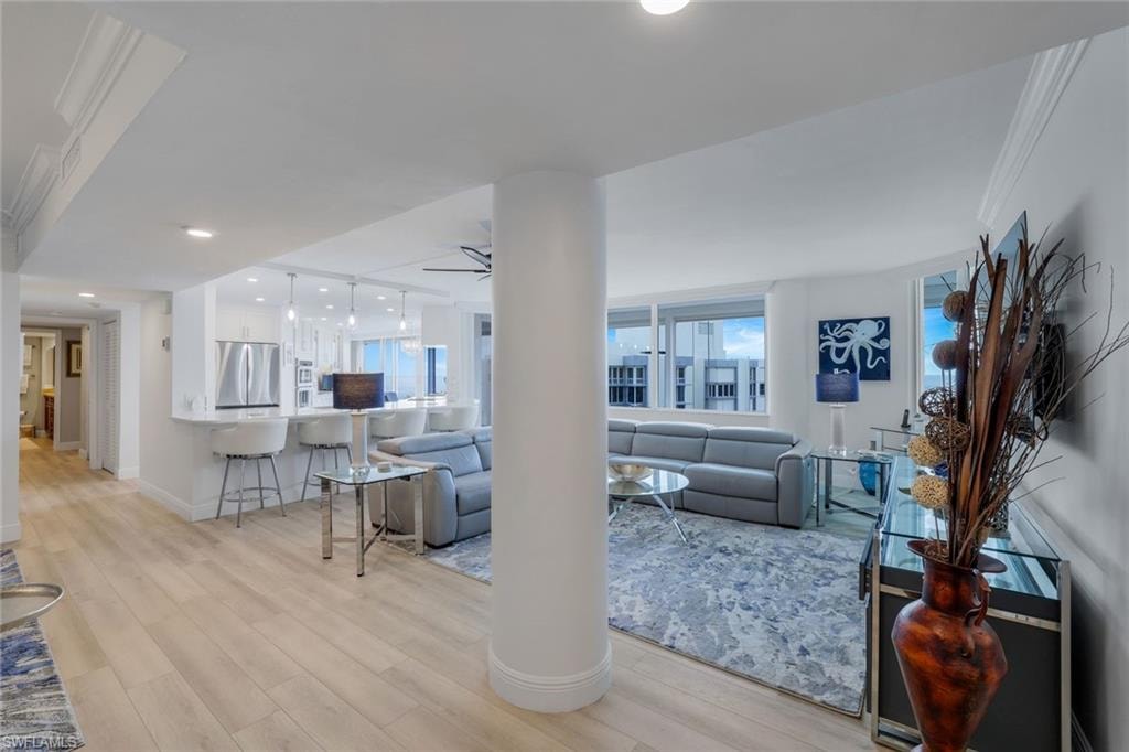 Living area featuring light wood-type flooring, a ceiling fan, ornamental molding, and baseboards