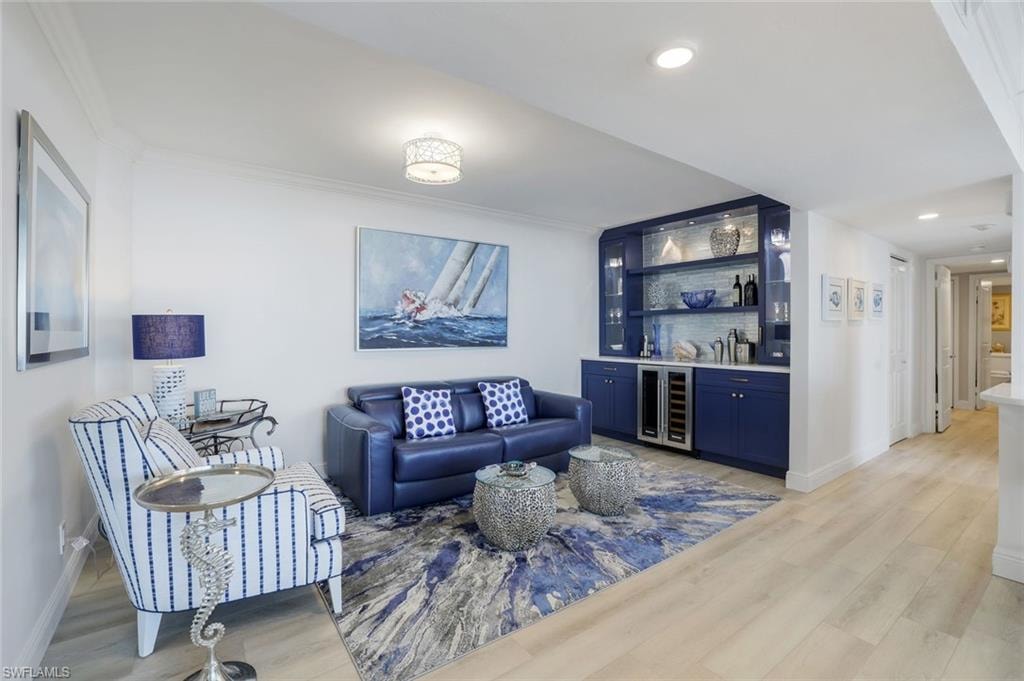 Living area with wine cooler, a dry bar, crown molding, baseboards, and light wood-style flooring
