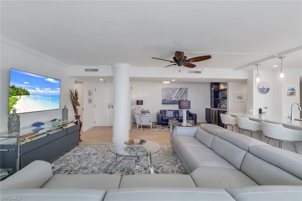 Living area with ceiling fan, light wood-style floors, ornate columns, and ornamental molding