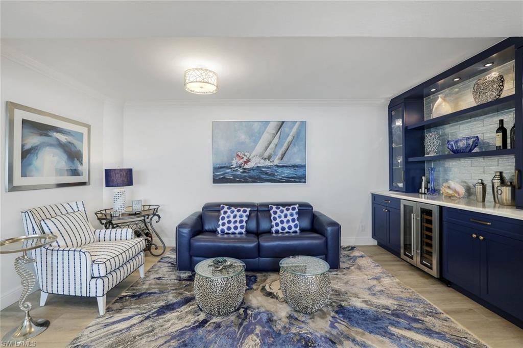 Living area with beverage cooler, ornamental molding, bar area, light wood-style floors, and baseboards