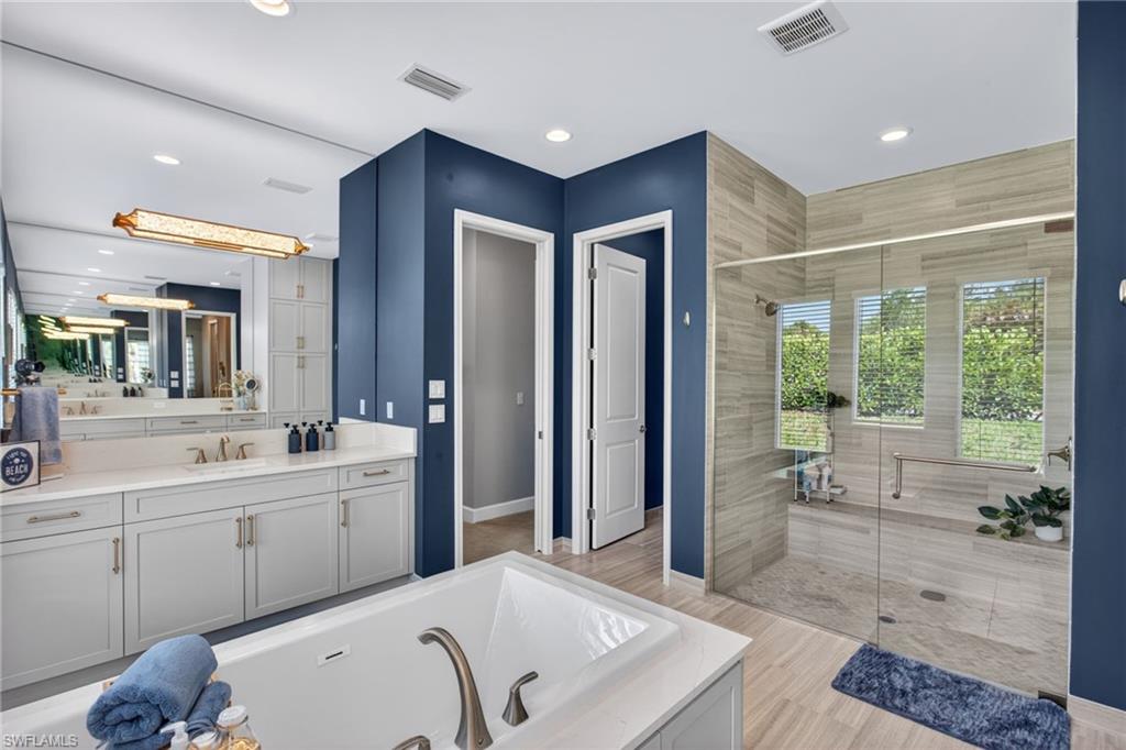 Soaking tub with brushed nickel fixtures, a spacious walk-in shower with natural light, a double vanity with ample counter space, custom cabinetry, and a large mirror