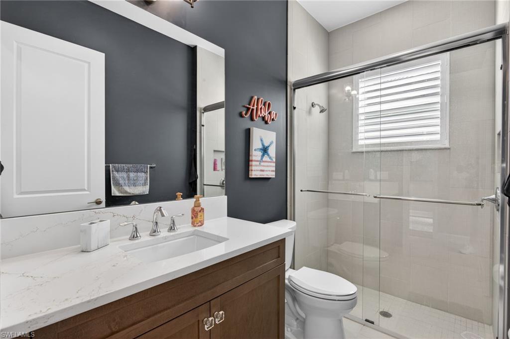 Bathroom featuring a wood-finish vanity with a quartz countertop, an undermount sink, and a framed mirror
