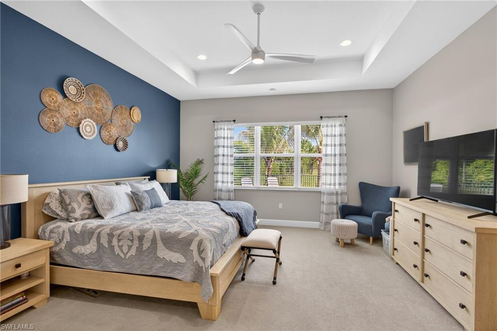 Recessed lighting illuminates a spacious room featuring a tray ceiling and a multi-pane window