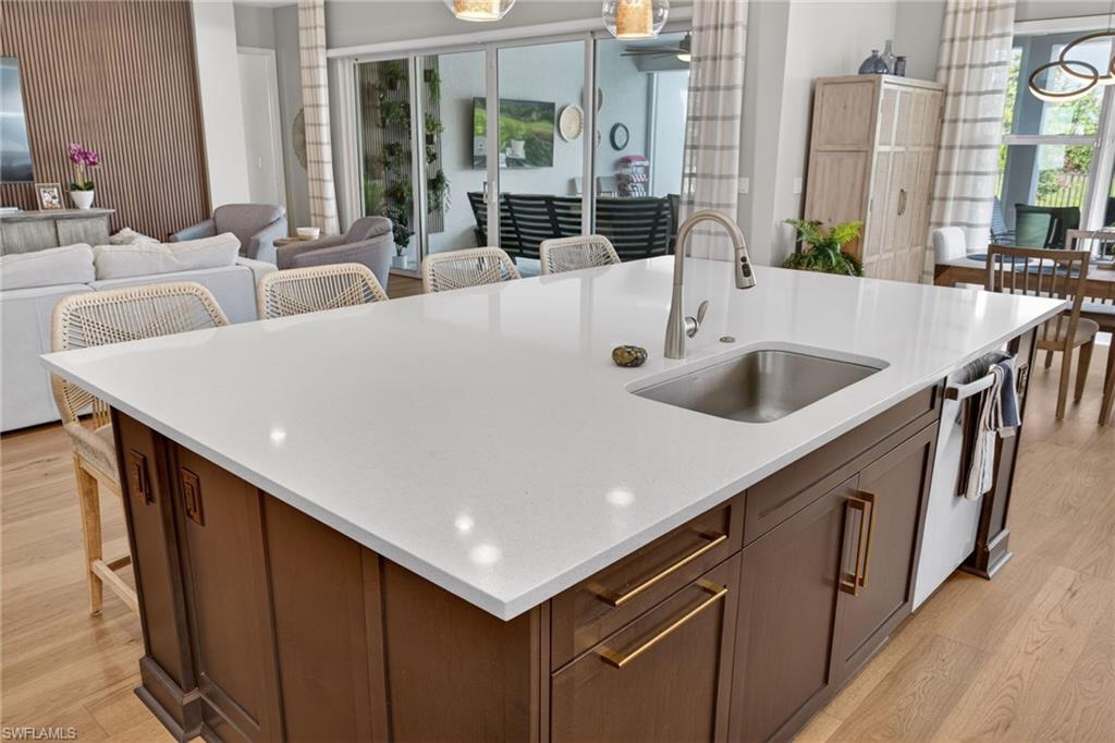 Kitchen island with a white countertop and integrated sink, featuring dark wood cabinetry with gold-tone hardware