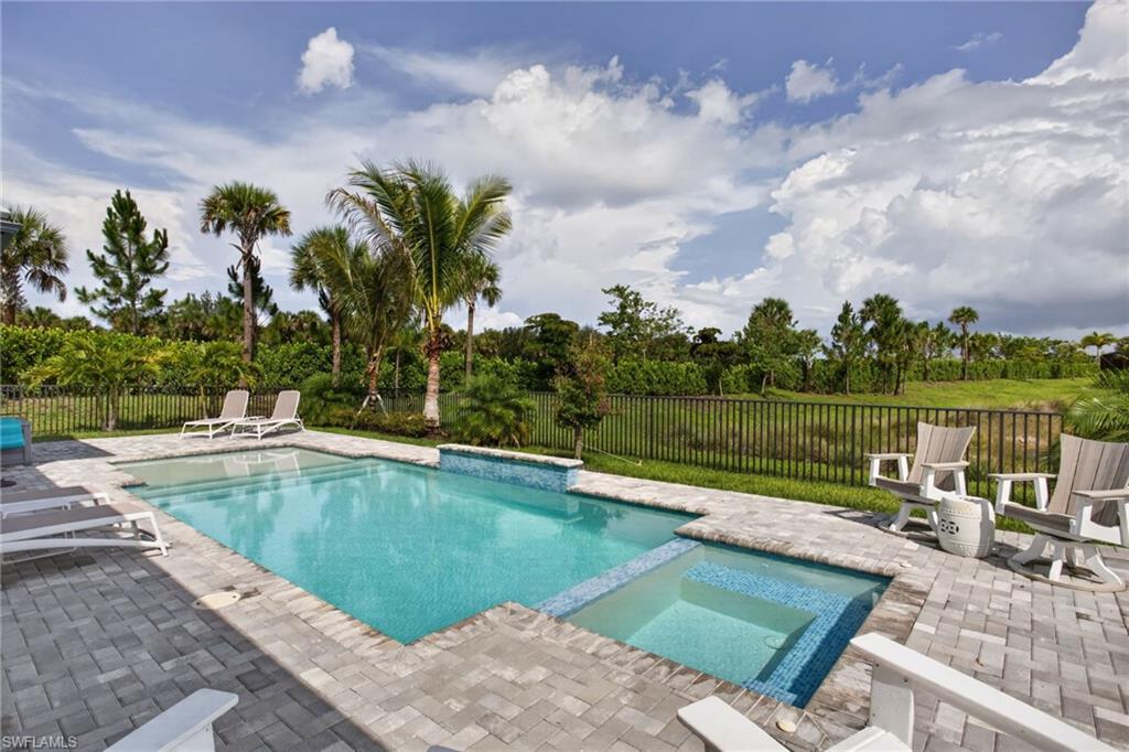 Expansive outdoor living area featuring a rectangular pool, integrated spa, paver patio, and lush tropical landscaping