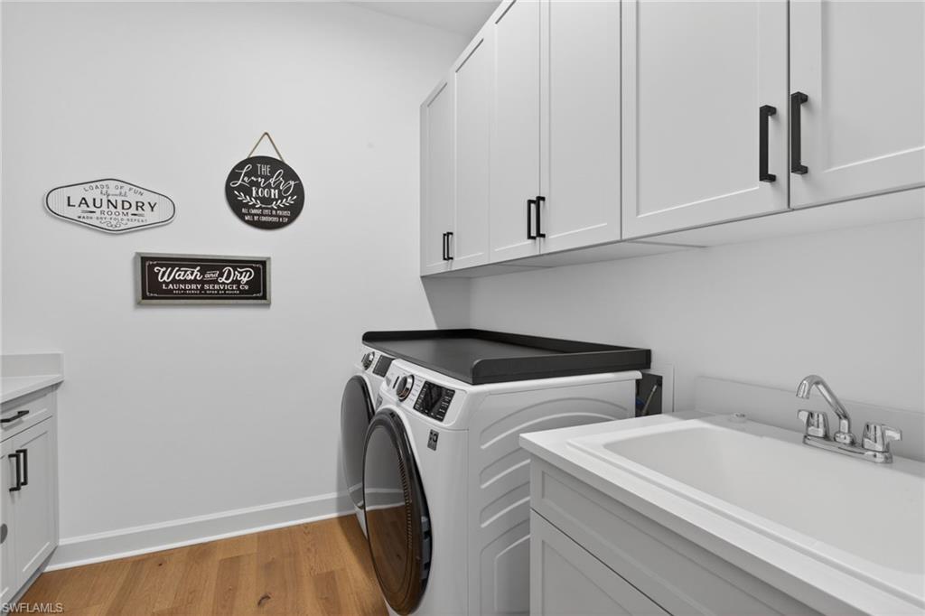Dedicated laundry room featuring light wood-finish flooring, white cabinetry with matte black hardware, and a utility sink with a chrome faucet