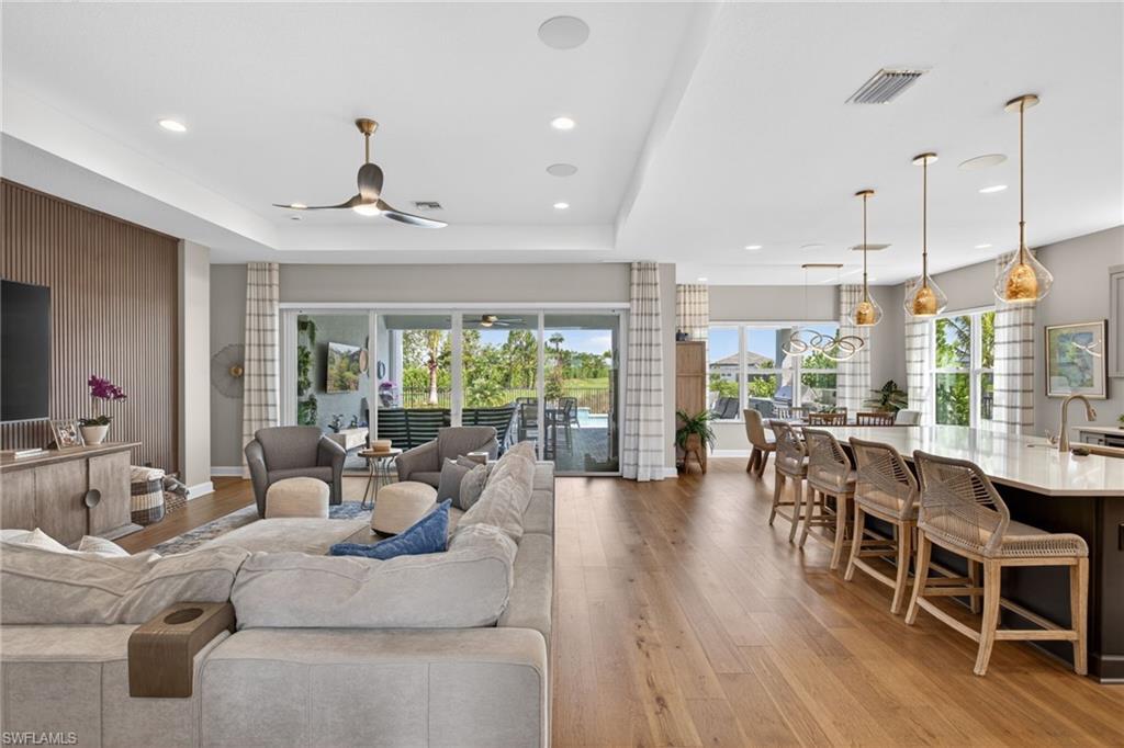 Spacious open-concept interior featuring wood-finish flooring, a contemporary kitchen island with seating, a decorative slatted wall accent, recessed lighting, and expansive glass sliders leading to an outdoor area