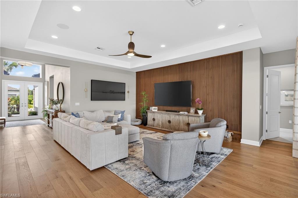 Open-concept living area featuring wood-finish flooring, a tray ceiling with recessed lighting, and a modern ceiling fan