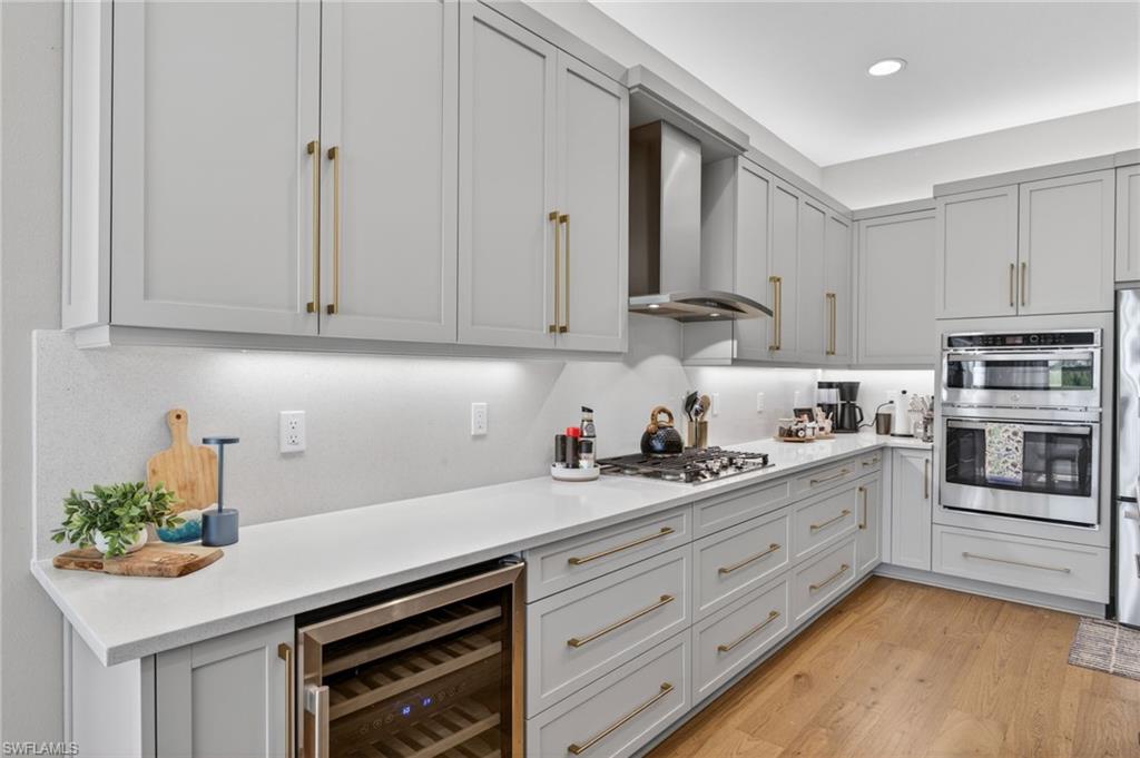 Modern kitchen featuring light gray shaker cabinetry with gold-tone hardware, white countertops, and a full suite of stainless steel appliances including a built-in oven and microwave