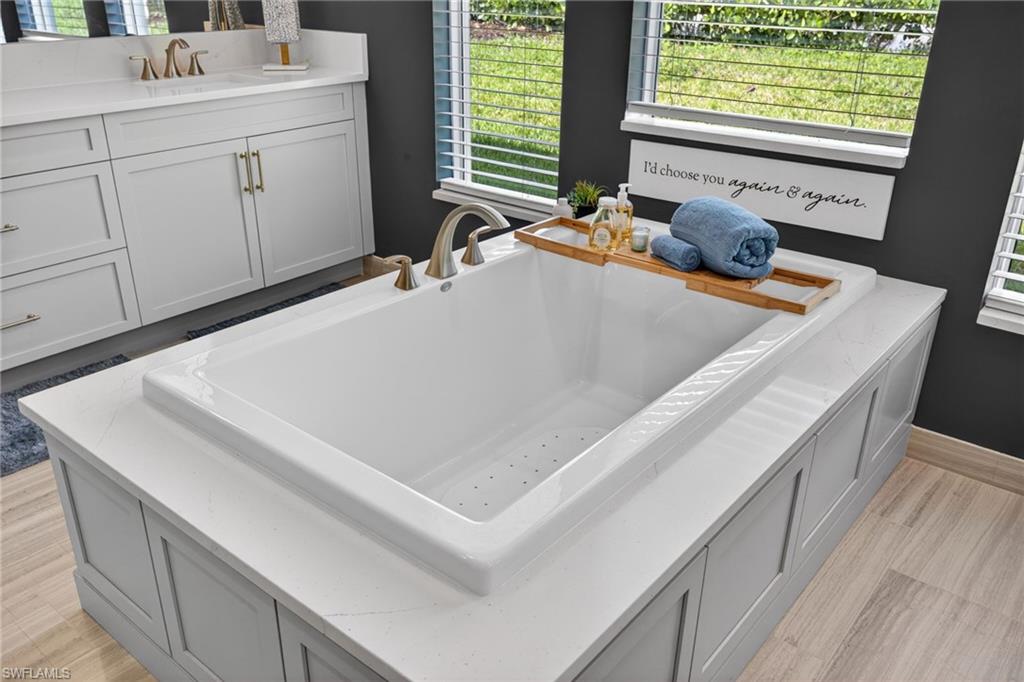 Built-in soaking tub with a light gray panel surround and a white stone-finish deck
