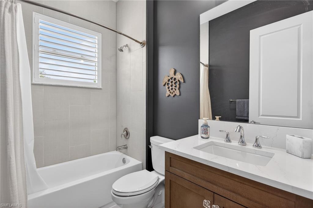 Bathroom featuring a white bathtub, light-toned wall tiling, a window with horizontal blinds, a dark accent wall, and a vanity with a white countertop and a built-in sink