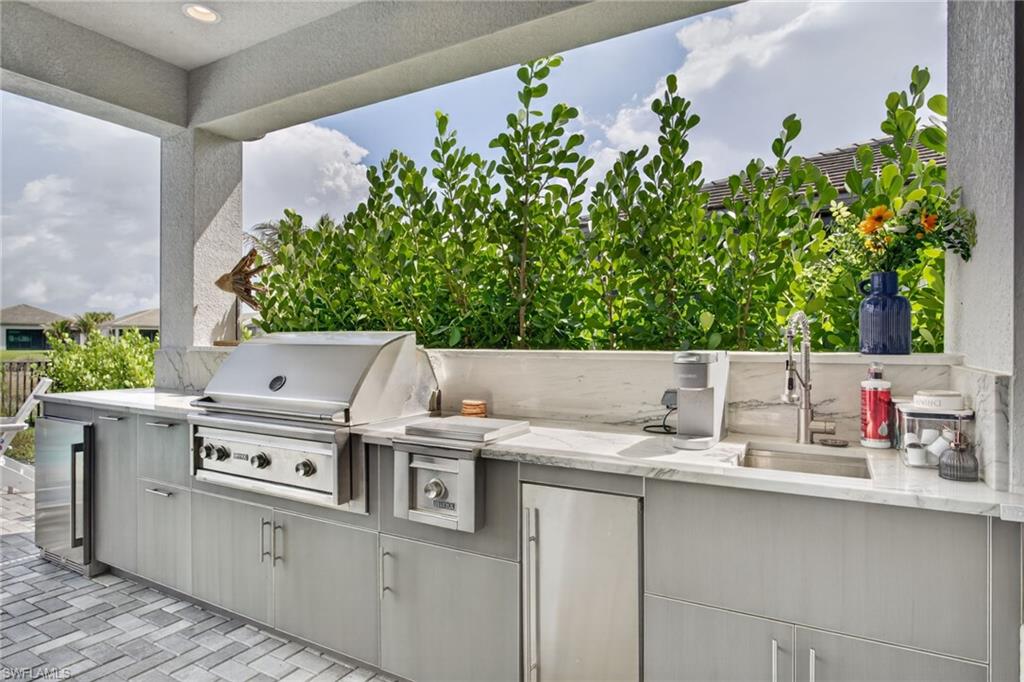 Outdoor kitchen featuring a built-in stainless steel grill, integrated sink with faucet, under-counter refrigeration, and stone countertops