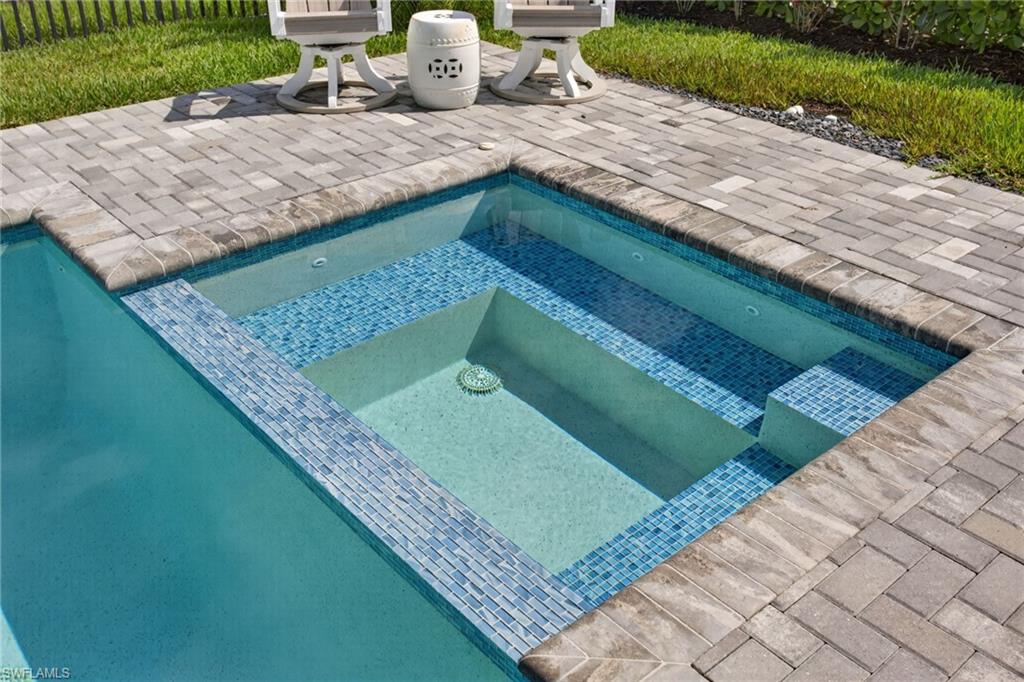 Outdoor pool area featuring a spa with blue mosaic tile accents, integrated steps, and a paver deck