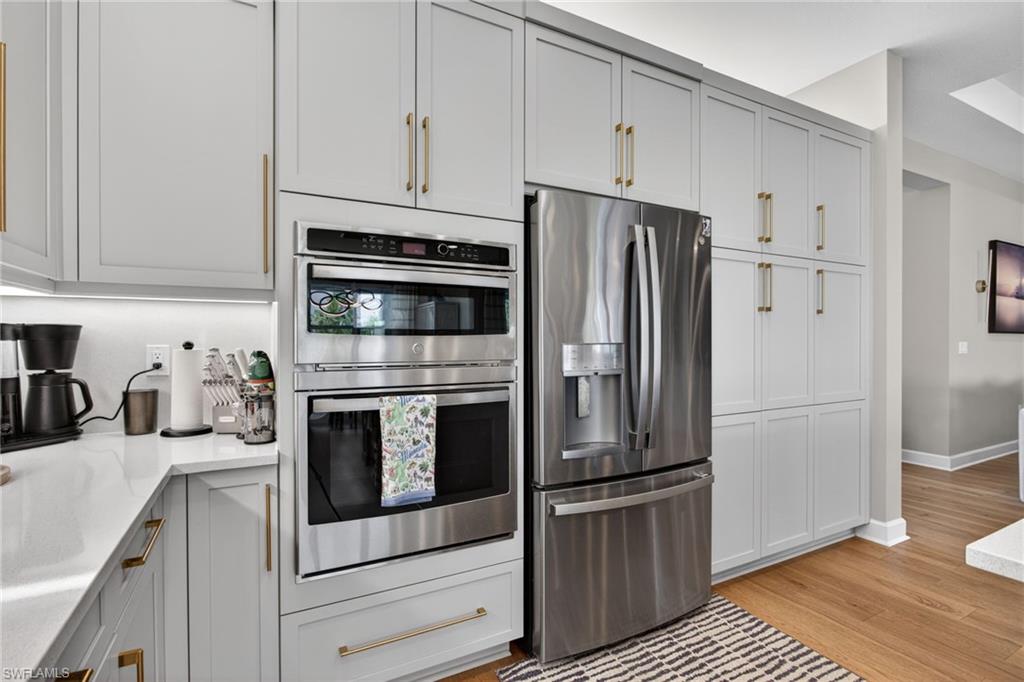 Modern kitchen featuring light gray cabinetry, gold-tone hardware, stainless steel appliances, and a built-in oven and microwave