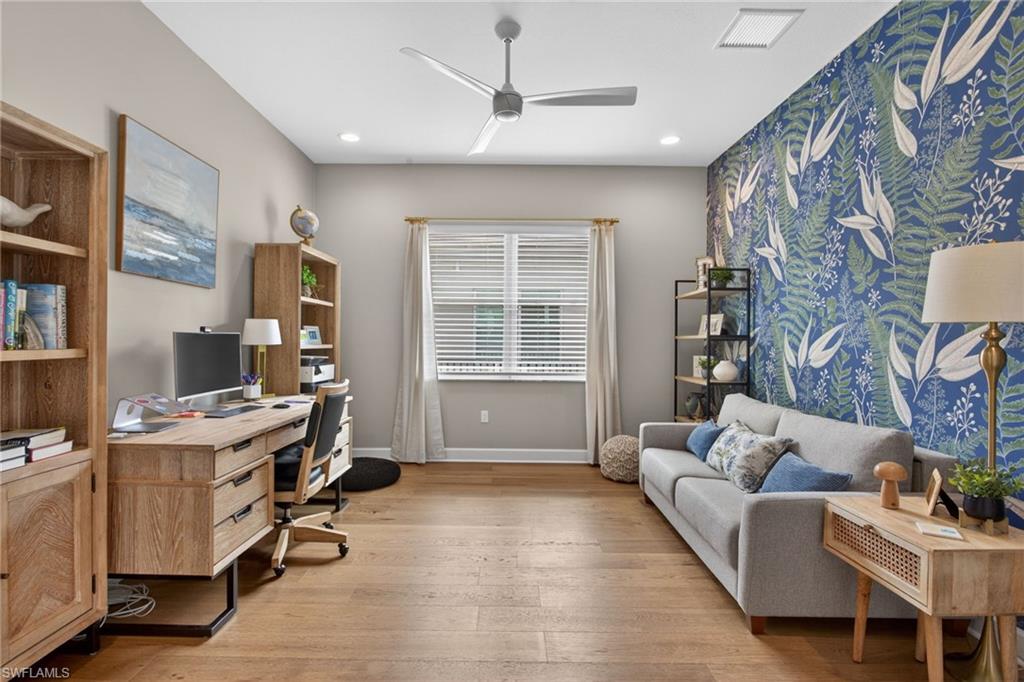 Expansive room featuring wood-finish flooring, a contemporary ceiling fan, recessed lighting, and a prominent accent wall with botanical-patterned wallpaper