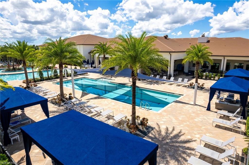 Expansive paver pool deck featuring multiple swimming pools, mature palm trees, and shaded cabanas