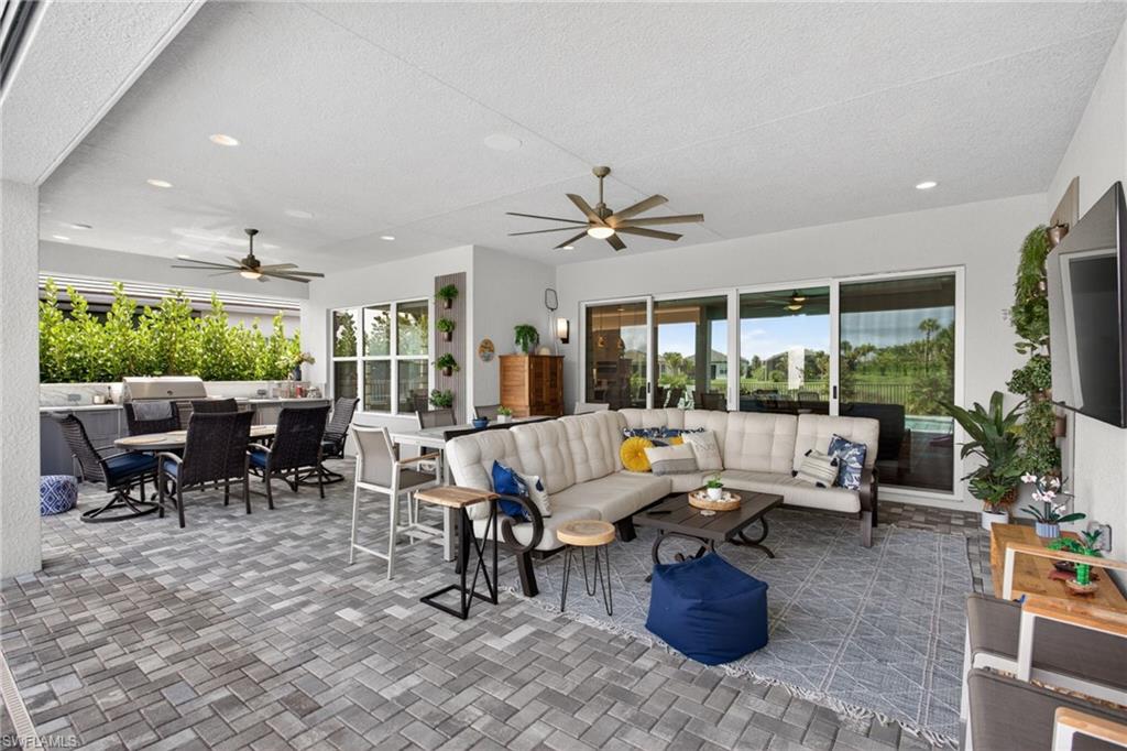 Expansive covered patio featuring paver flooring, multiple ceiling fans, recessed lighting, an outdoor kitchen with integrated grill, and a wall of sliding glass doors