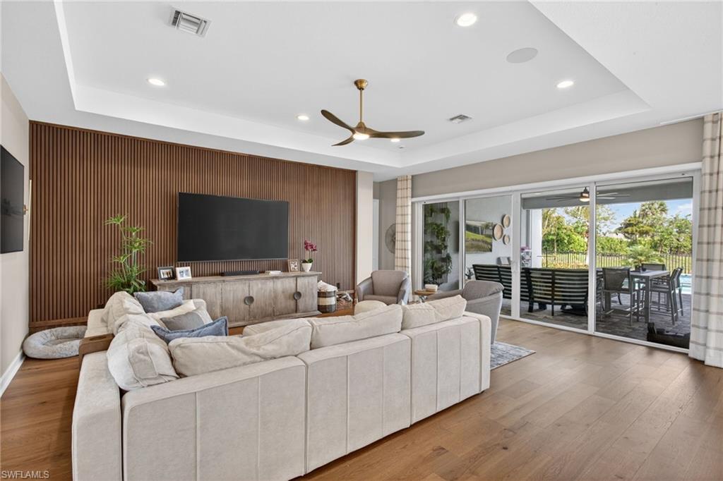 Spacious living area featuring wood-finish flooring, a tray ceiling with recessed lighting, and a modern ceiling fan