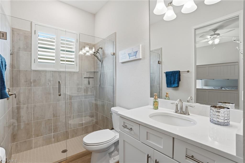 Bathroom featuring a glass-enclosed shower with large format tile surround, a white vanity with a single basin sink, a large wall-mounted mirror, and a window with plantation shutters