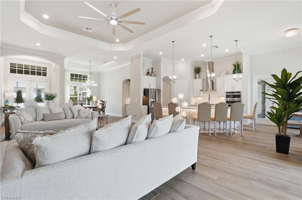 Open-concept main living area with wood-finish flooring, tray ceiling, recessed lighting, and ceiling fan