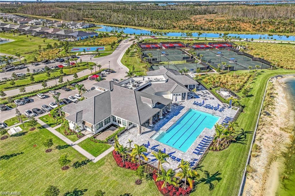 Community clubhouse with a large outdoor swimming pool, adjacent tennis courts, and landscaped grounds