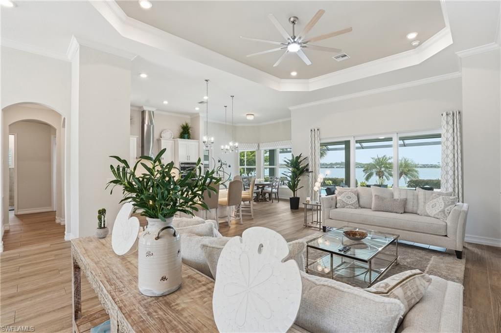 Open-concept living area featuring a tray ceiling with recessed lighting and a ceiling fan, wood-finish flooring, and expansive windows offering water frontage