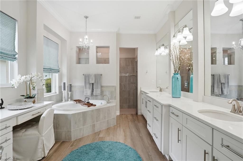 Spacious bathroom featuring a corner soaking tub with tile surround, dual vanity with undermount sinks and quartz-style countertops, wood-finish flooring, and a separate walk-in shower