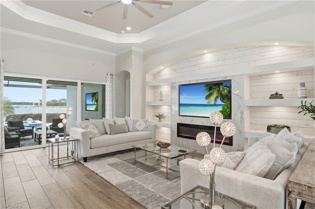 Living area featuring wood-finish flooring, a tray ceiling with a fan, and crown molding