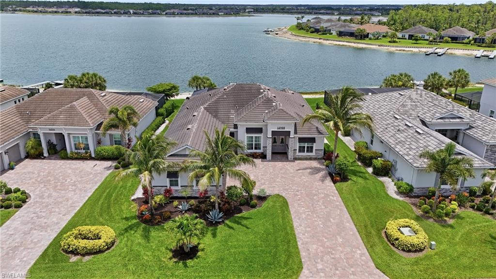 Waterfront property featuring a paver driveway, mature palm trees, manicured landscaping, and a tile roof