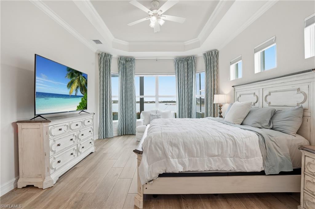 Tray ceiling with a ceiling fan, wood-finish flooring, and multiple windows with water scenery
