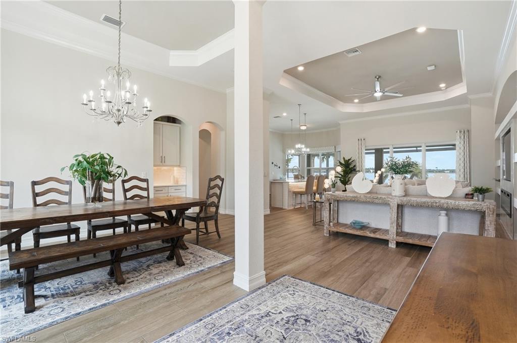 Open-concept interior featuring wood-finish flooring, tray ceilings with recessed lighting, and a prominent chandelier