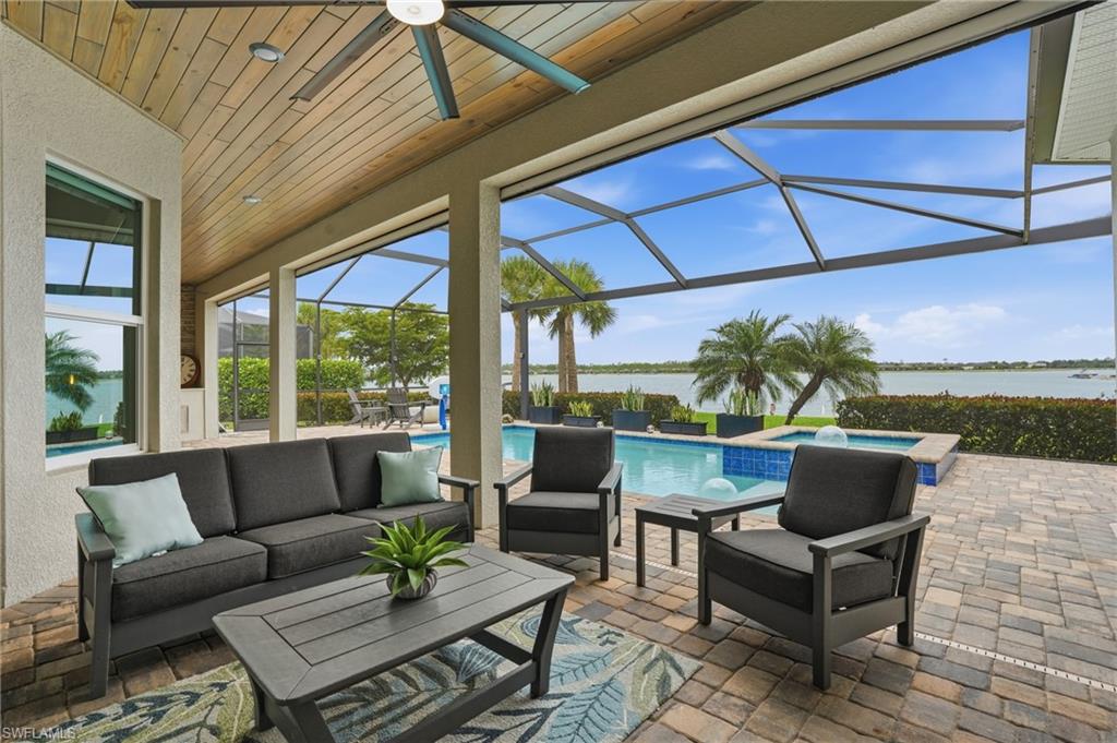 Spacious screened lanai featuring a wood-finish ceiling, ceiling fan, paver flooring, and direct access to a swimming pool with an integrated spa, all overlooking a body of water