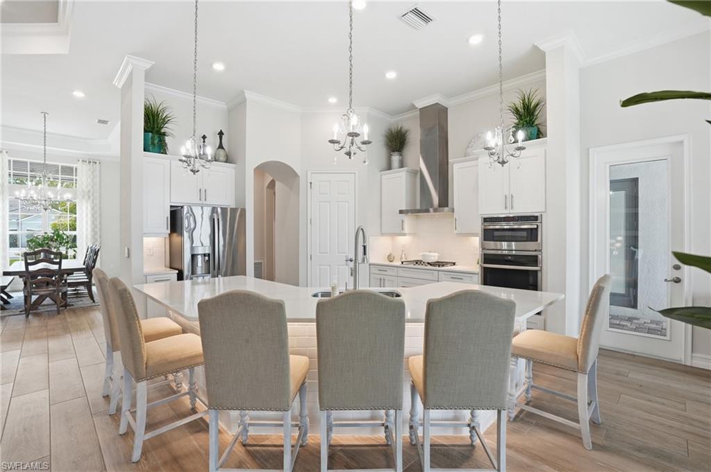 Gourmet kitchen featuring a large island, contemporary pendant lighting, stainless steel appliances, stacked wall oven, and wood-finish flooring