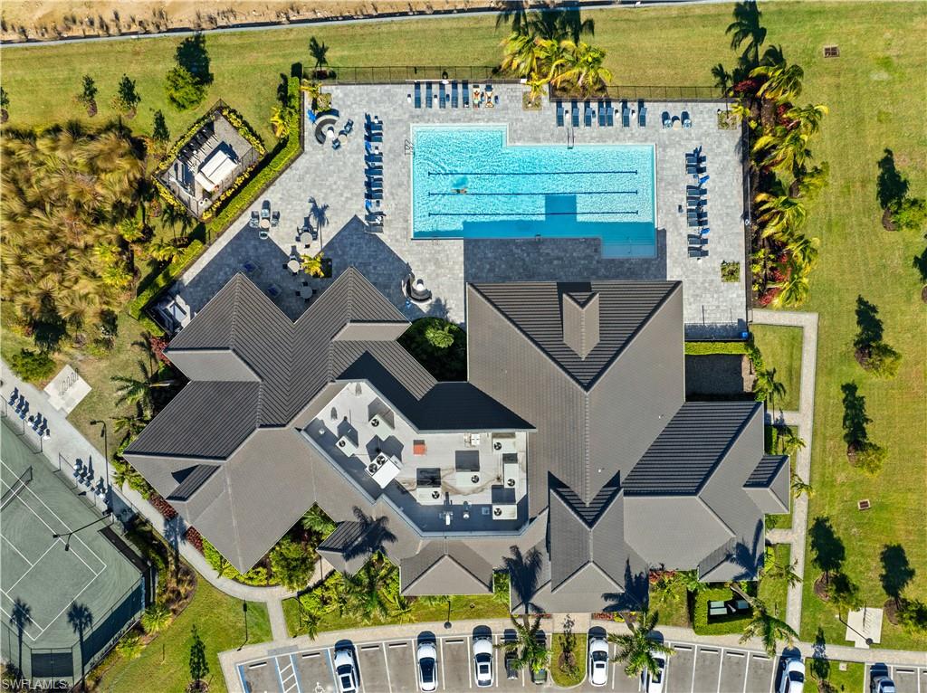 Community clubhouse with a gabled roofline, adjacent swimming pool, dedicated lap lanes, ample sundeck seating, and tennis courts