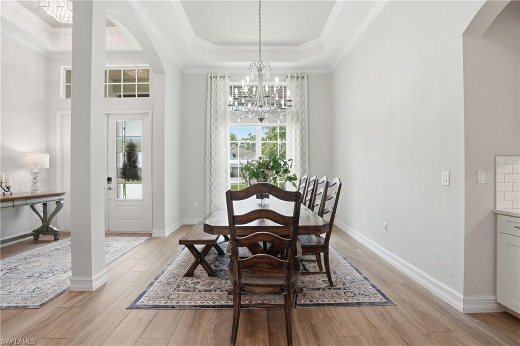 Formal dining area featuring wood-finish flooring, a tray ceiling with crown molding, and a chandelier