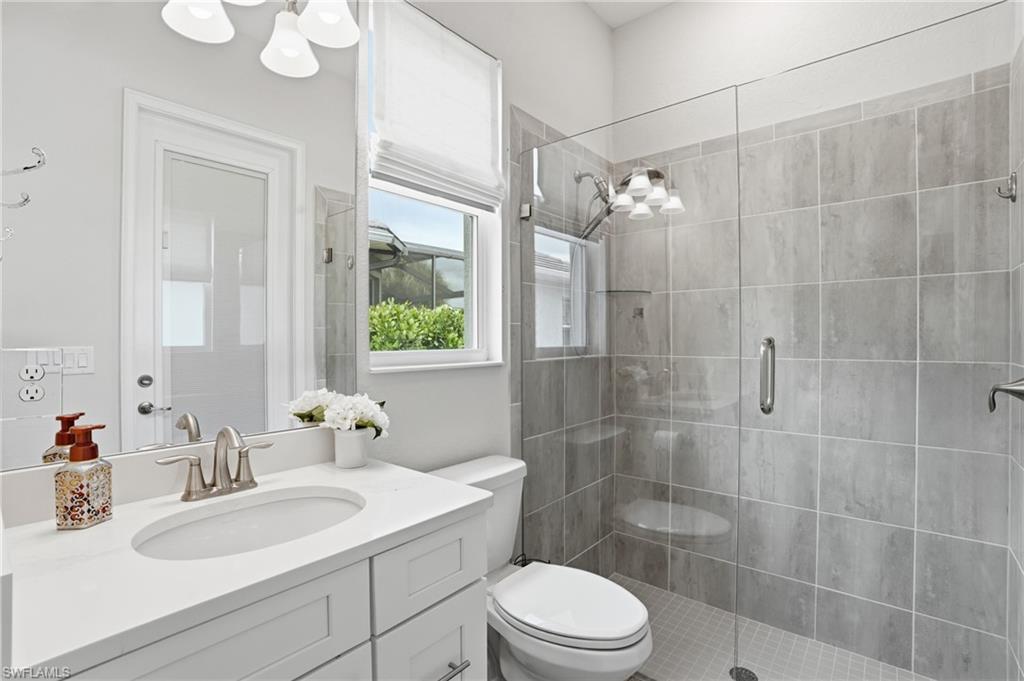 Tiled shower with a clear glass enclosure and built-in shelving, complemented by a white vanity with an undermount sink and polished chrome faucet