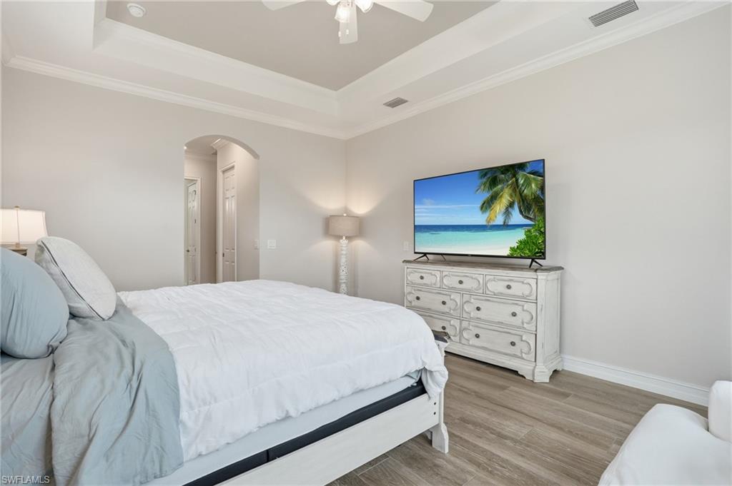 Tray ceiling with crown molding, wood-finish flooring, recessed lighting, and arched doorway