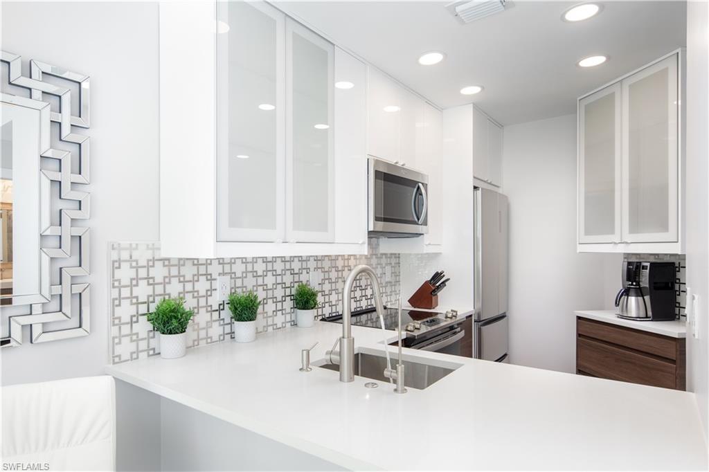 Contemporary kitchen featuring white cabinetry, stainless steel appliances, a geometric tile backsplash, recessed lighting, and white countertops