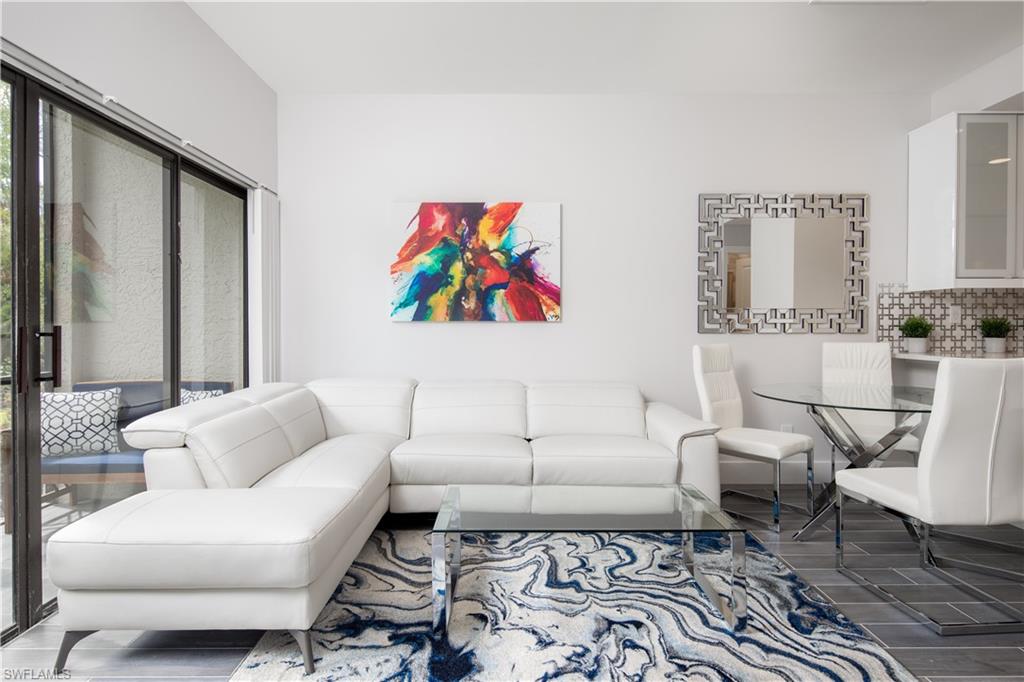 Open-concept living space featuring high ceilings, dark-framed sliding glass doors, contemporary tile flooring, a geometric tile backsplash, and white cabinetry